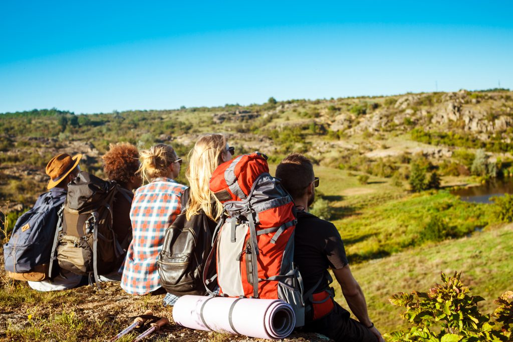 jóvenes sentados en una loma, visualizando el paisaje que les rodea
